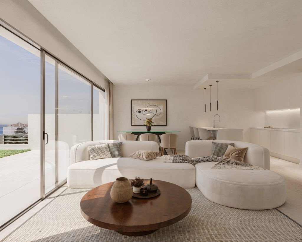 Modern living room with a large white sectional sofa, coffee table, and sliding glass doors opening to a sea view terrace.