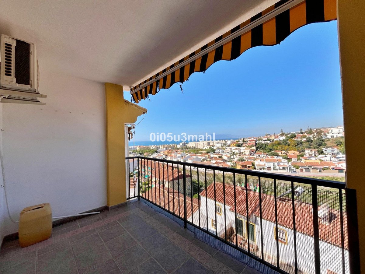 A balcony with a railing offers a view of a coastal town and the sea under a clear blue sky.