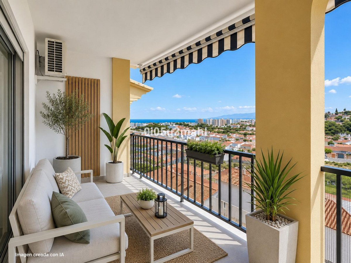 A modern balcony with comfortable seating, coffee table, plants, and a scenic view of the sea and cityscape below town.