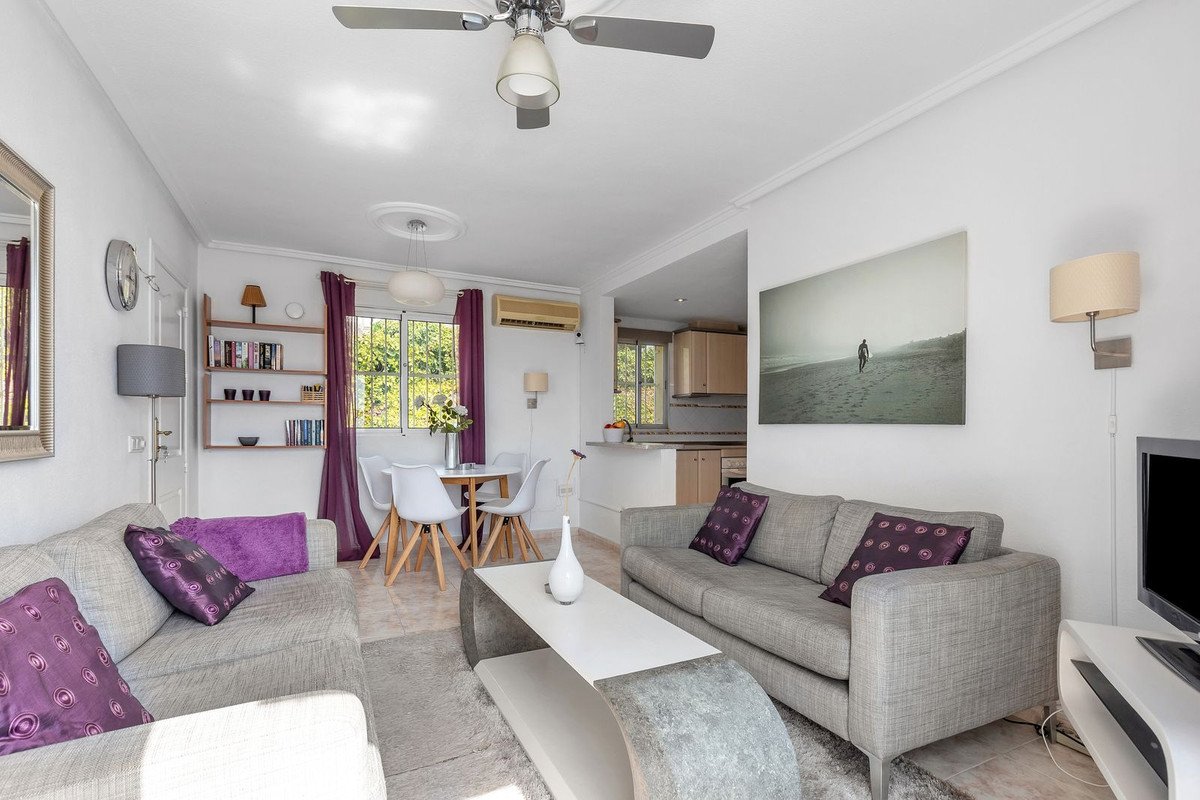 A comfortable living and dining area with grey sofas, a white table, and modern chairs, featuring a large window with purple curtains.