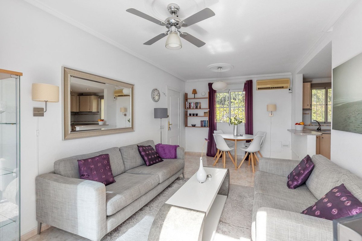Bright living room with grey sofas, dining area with white chairs, and large window with purple curtains.