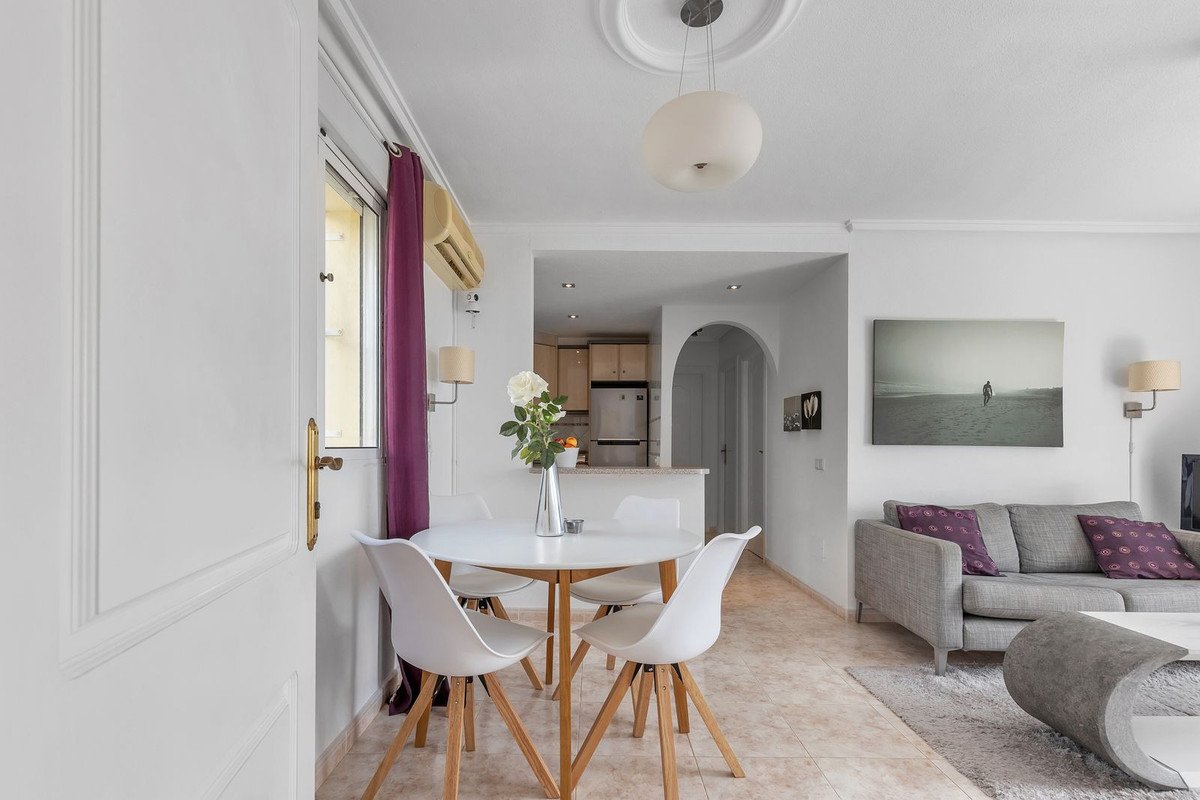 Modern living and dining area with white chairs, a round table, and a grey sofa with decorative pillows.