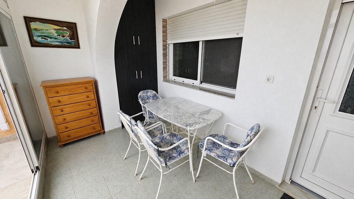 A small balcony with a dining set, a wooden dresser, and an ocean-themed painting on the wall.