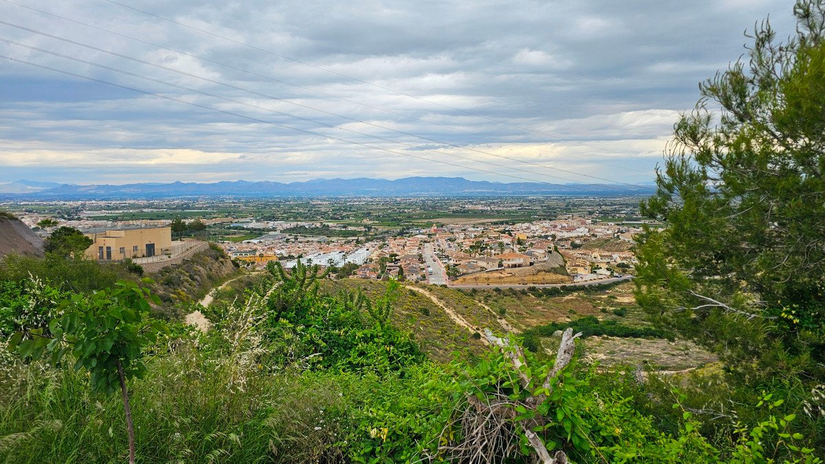 Panoramic view of a town nestled in a valley, with mountains in the distance under a cloudy sky.