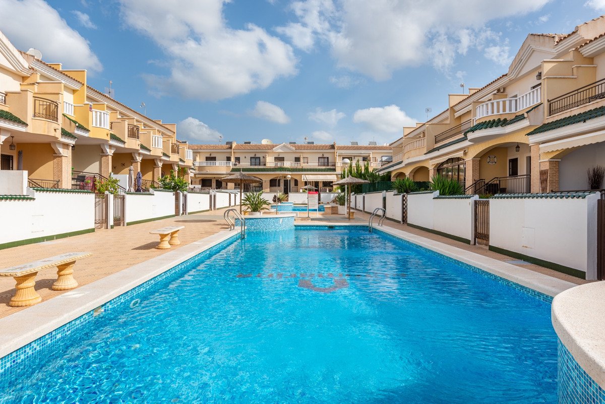 A wide view of a sparkling blue swimming pool with tiled edges, surrounded by townhouses and outdoor seating areas.