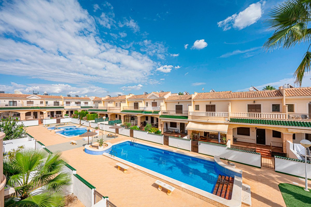 Apartment complex with multiple swimming pools and sun loungers under a bright blue sky with clouds.