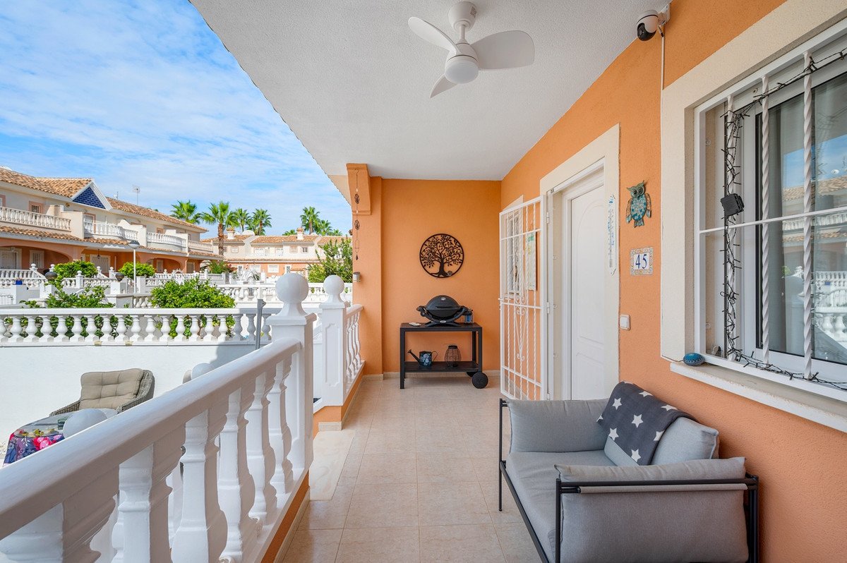 A covered terrace with a grill, sofa, and outdoor seating, overlooking a residential area with palm trees.