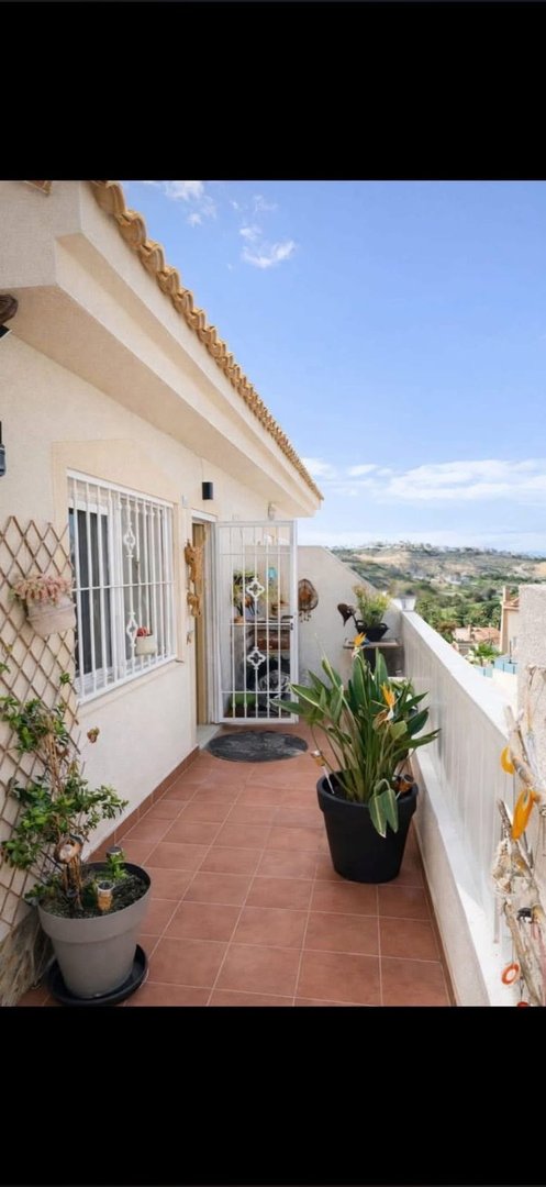 Terrace with plants, a white railing, a gated doorway, and a scenic view of hills under a blue sky.