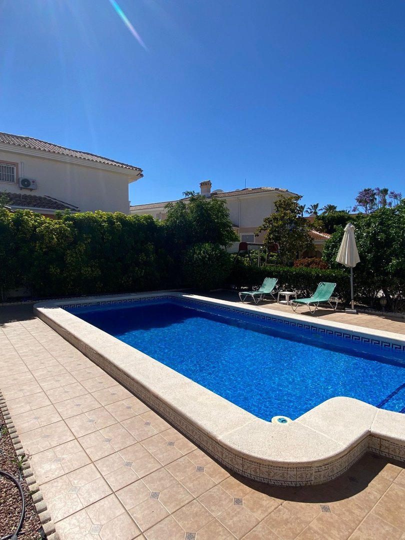 A private swimming pool with bright blue water, surrounded by tiled patio and lounge chairs, perfect for relaxation under the sun.