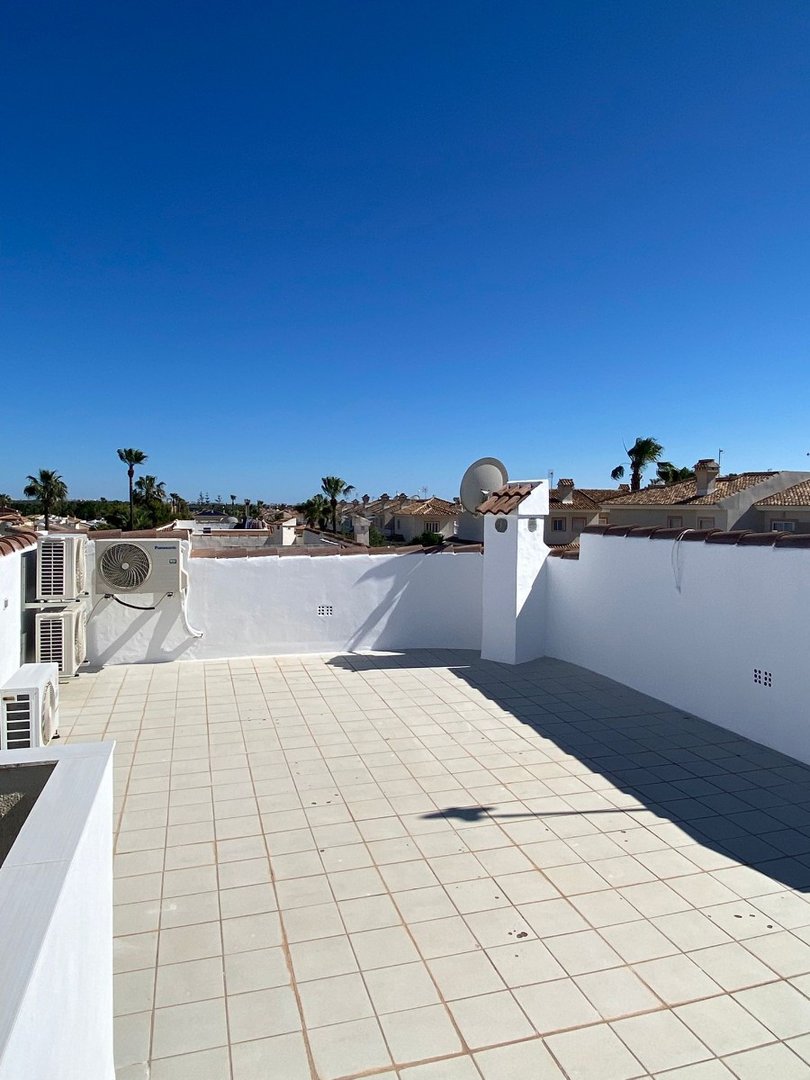 Spacious tiled terrace with white walls, air conditioning units, and a clear blue sky overhead. Views of rooftops and palm trees.