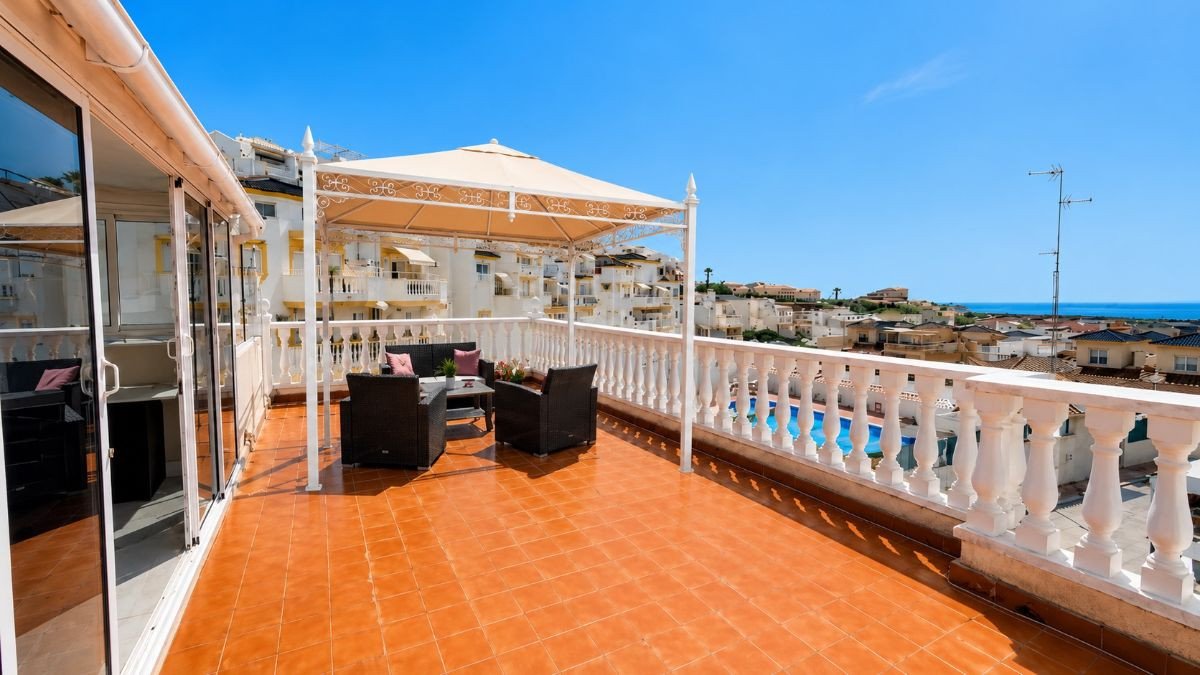 A spacious terrace with seating area, offering a beautiful view of the sea and residential buildings under a clear blue sky.