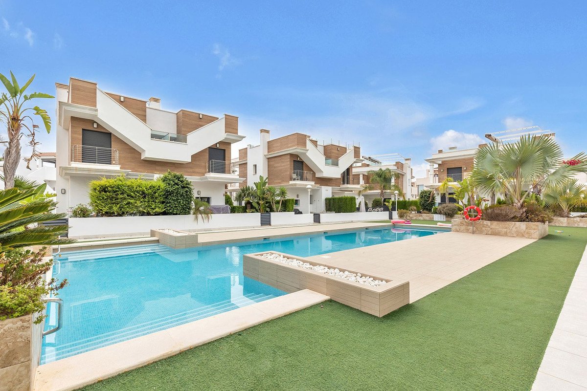 Modern villas with a communal swimming pool and green lawn area under a clear blue sky.