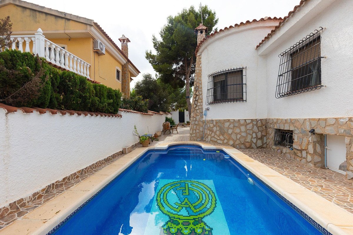 A private swimming pool with a decorative mosaic at the bottom, surrounded by a stone patio and a white wall.