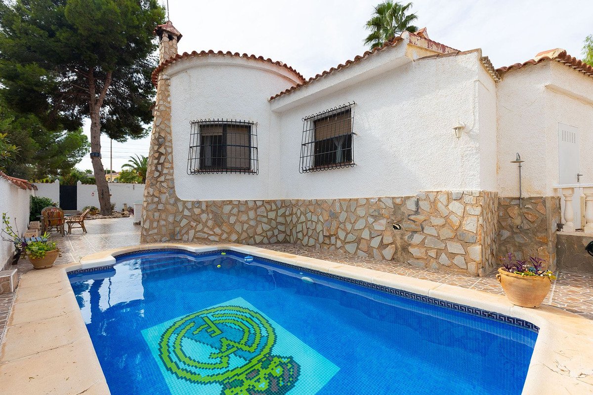 A bright blue swimming pool with a mosaic tile design at the bottom, next to a white house with stone accents.