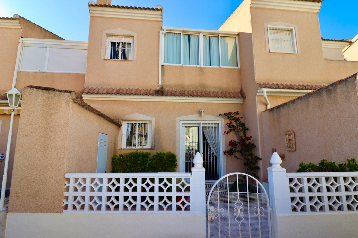 A light peach townhouse with a white balustrade and gate. Red flowers climb the wall near the entrance.