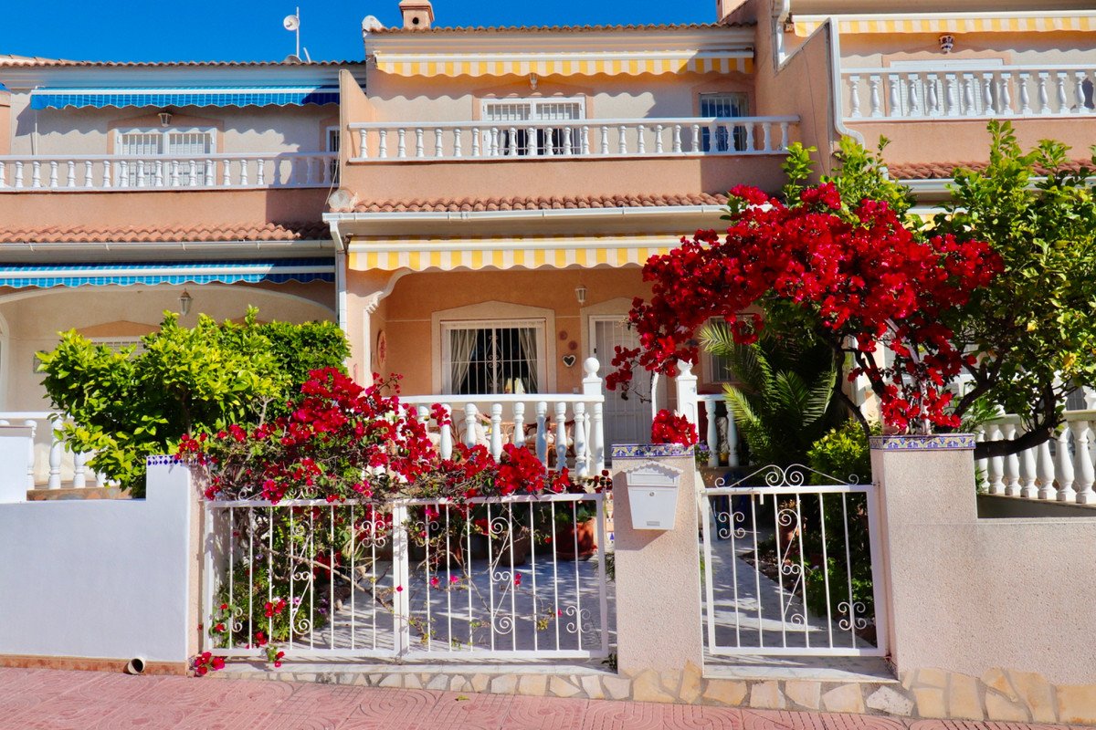 Villa with red bougainvillea, white railings, and striped awnings under a clear blue sky.