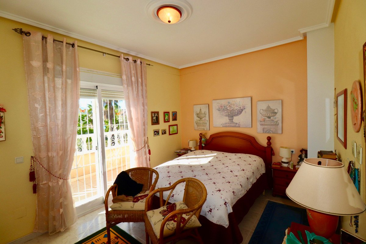 A bright bedroom with a double bed, balcony access with a view, and two wicker chairs.