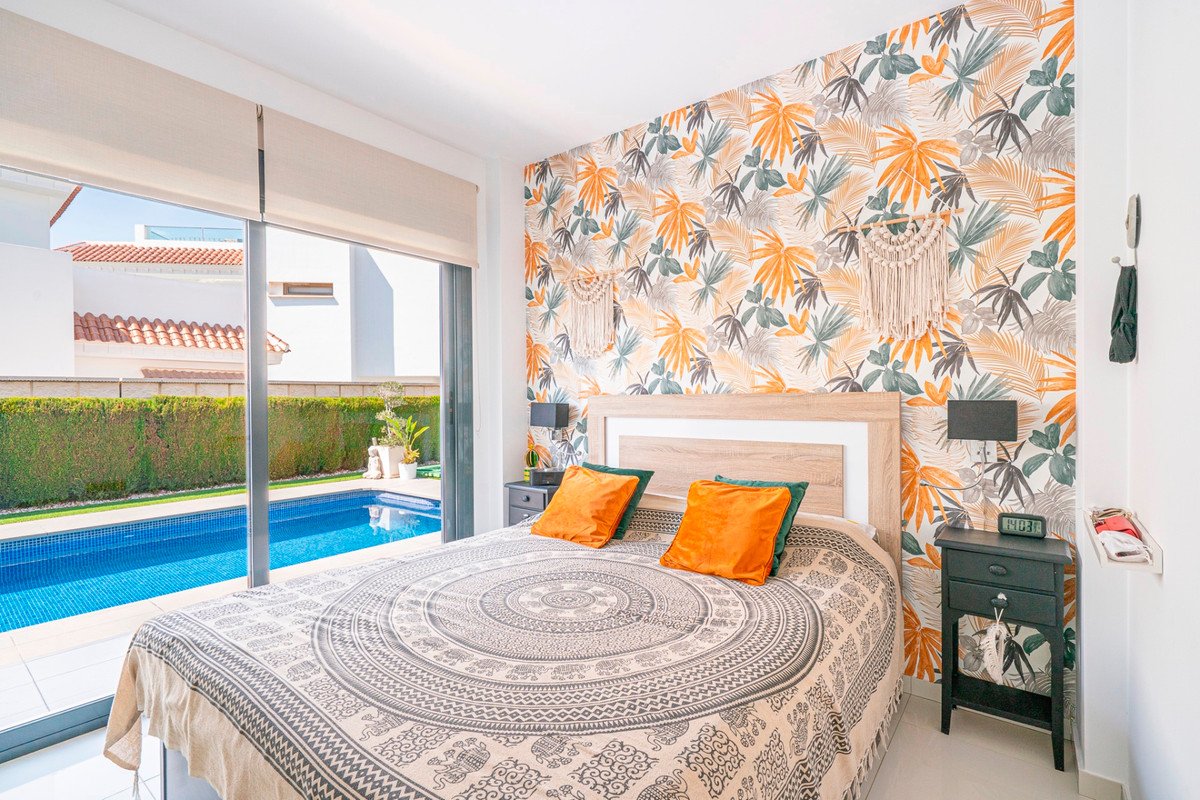 Bedroom with tropical wallpaper and a view of a private swimming pool through glass doors.