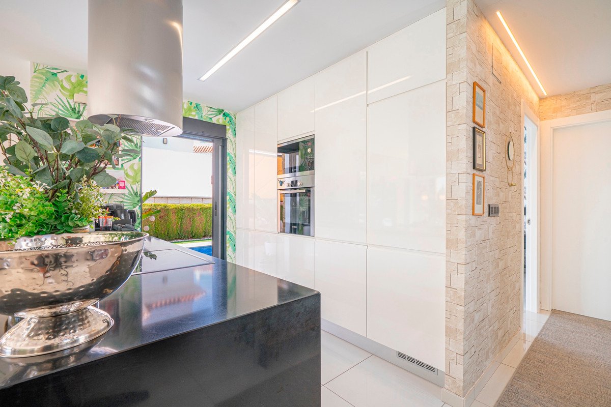 Modern kitchen featuring white high-gloss cabinets, black countertop, tropical wallpaper, and a view of an outdoor pool area.