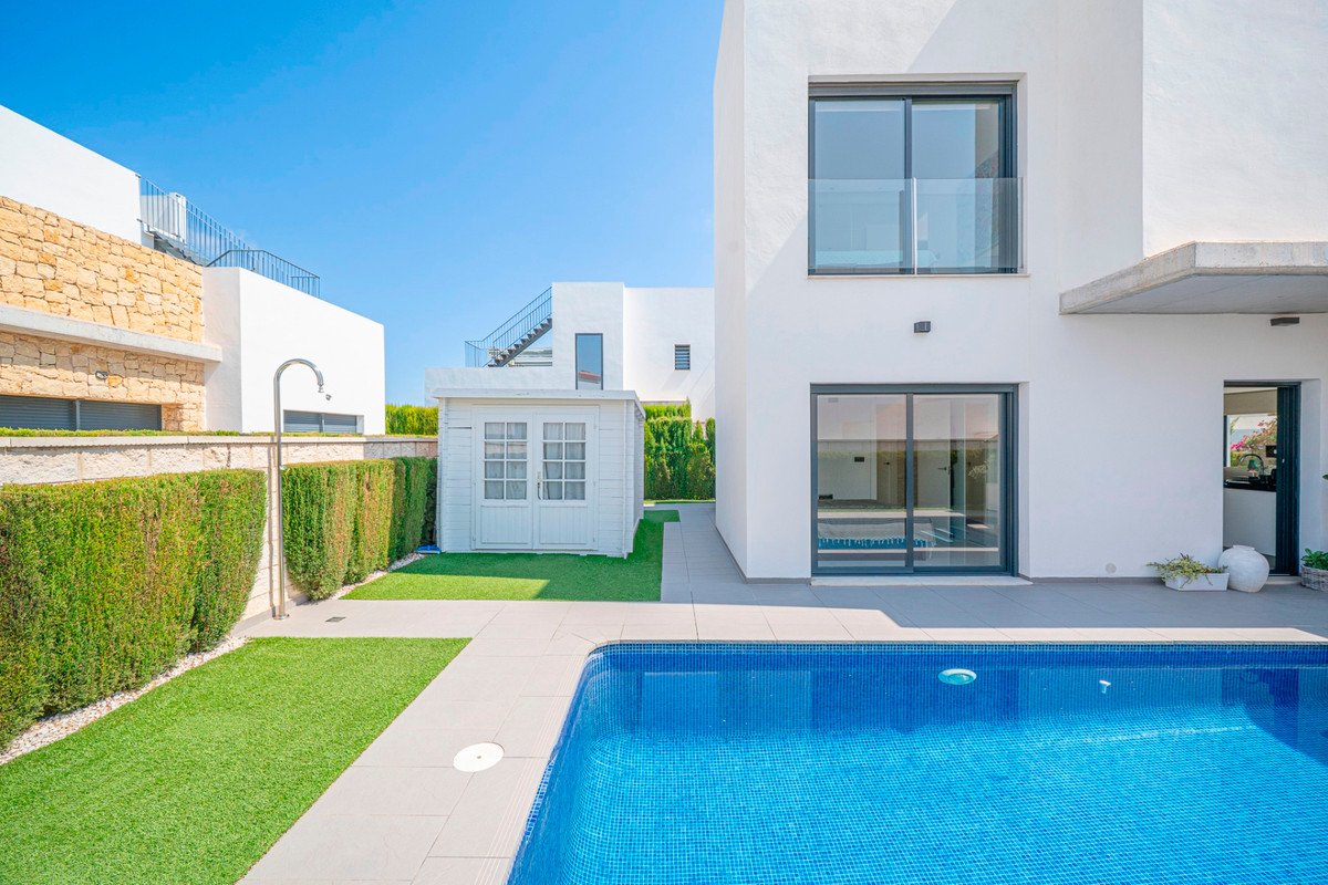 Modern white villa exterior with a blue tiled swimming pool, artificial lawn, and a small garden shed.
