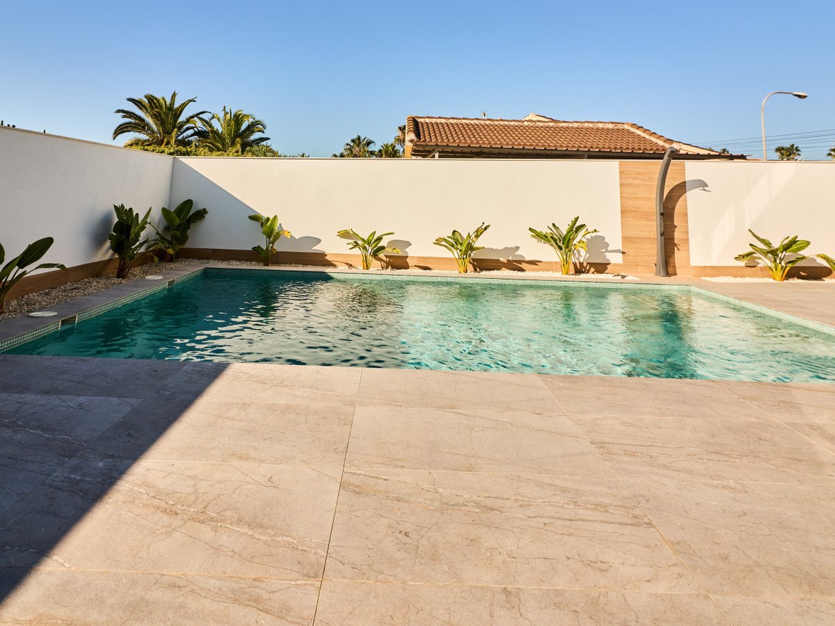 A sparkling private swimming pool with an outdoor shower and tropical plants, under a clear blue sky.