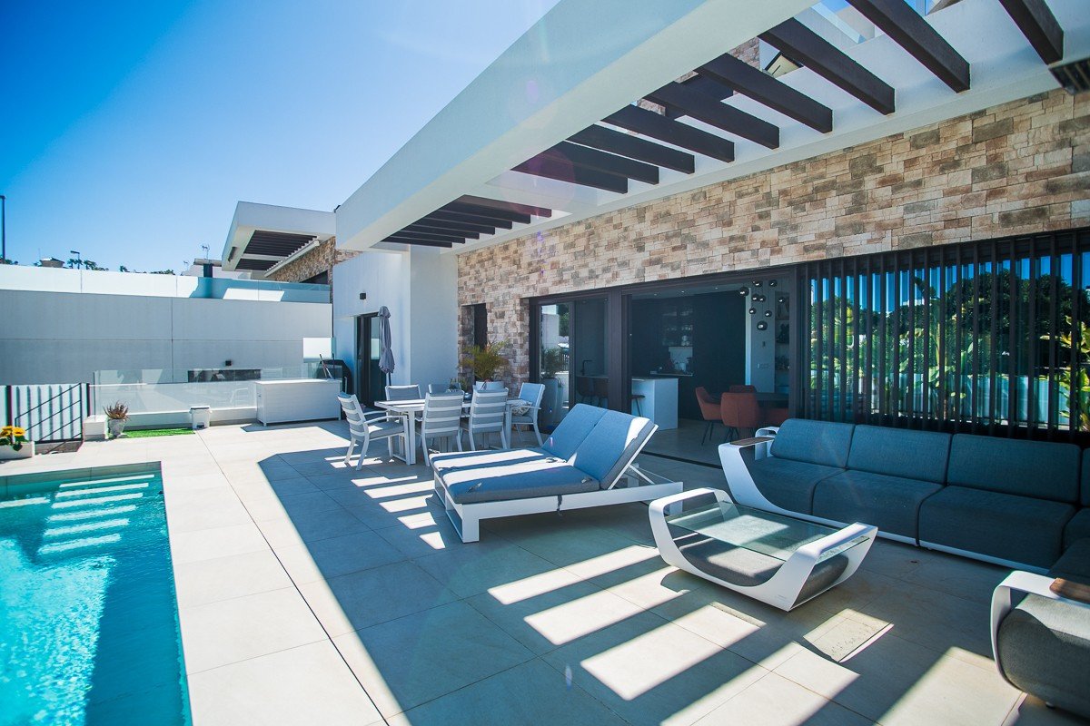 Spacious modern patio with a swimming pool, dining area, lounge seating, and an outdoor kitchen with stone accents.