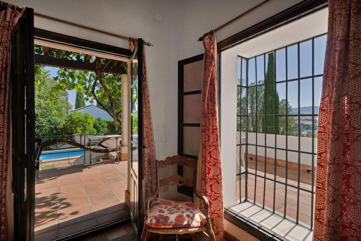 Balcony with pool view through open doors, featuring a wooden chair with floral cushion