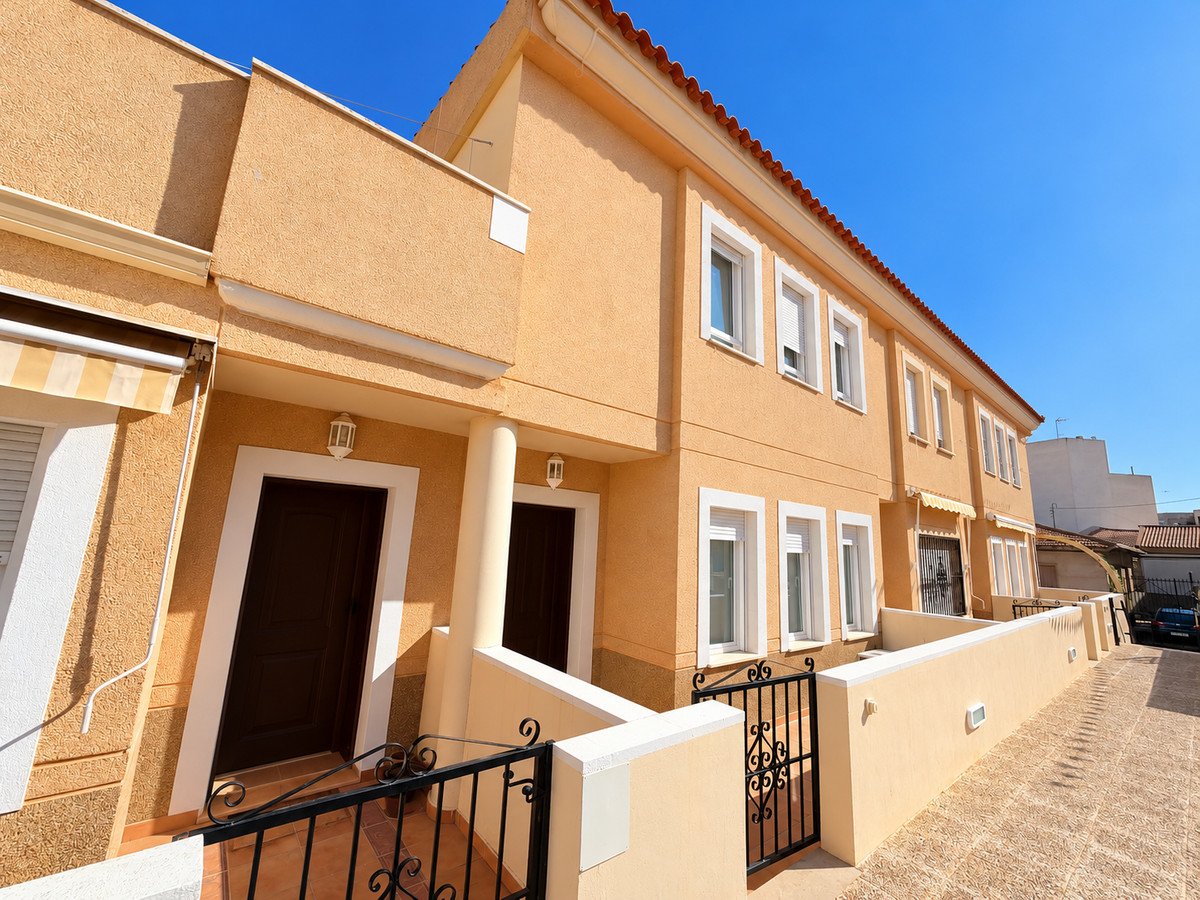 Townhouse with terracotta roof, white windows, and paved terrace under blue sky