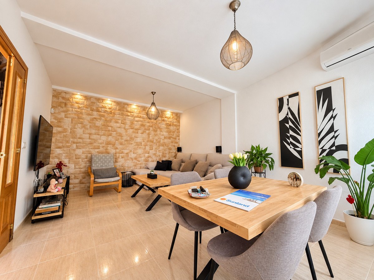Modern open-plan living and dining room with wooden table, sofa, stone accent wall, and plants