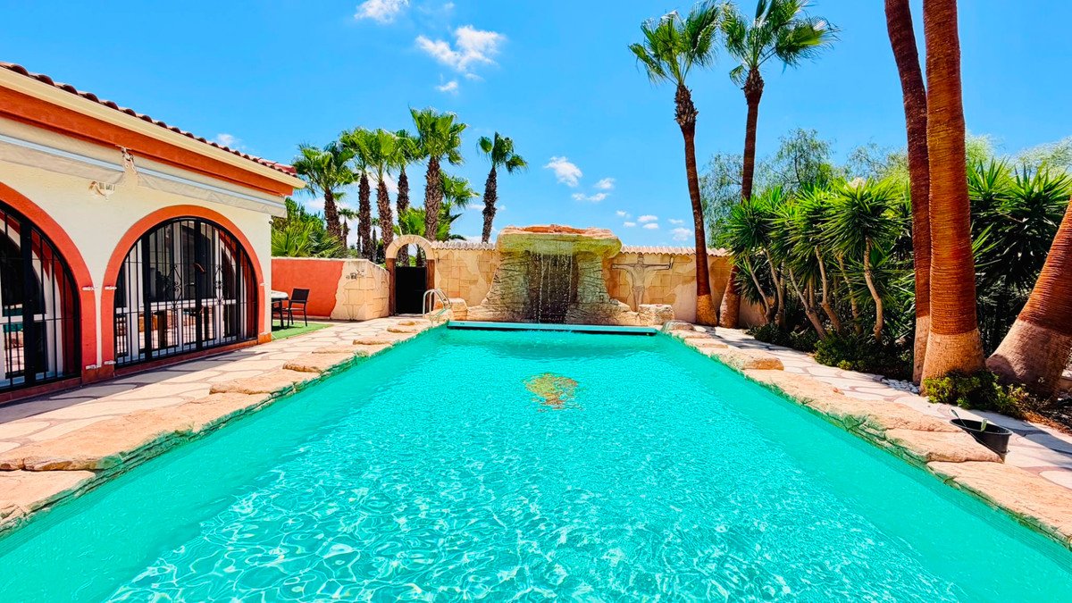 Backyard swimming pool with a waterfall feature and palm trees under a blue sky