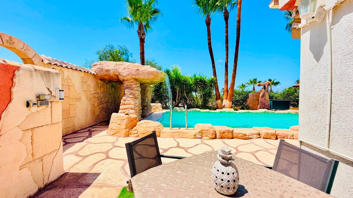 Outdoor patio with pool, palm trees, and stone water feature