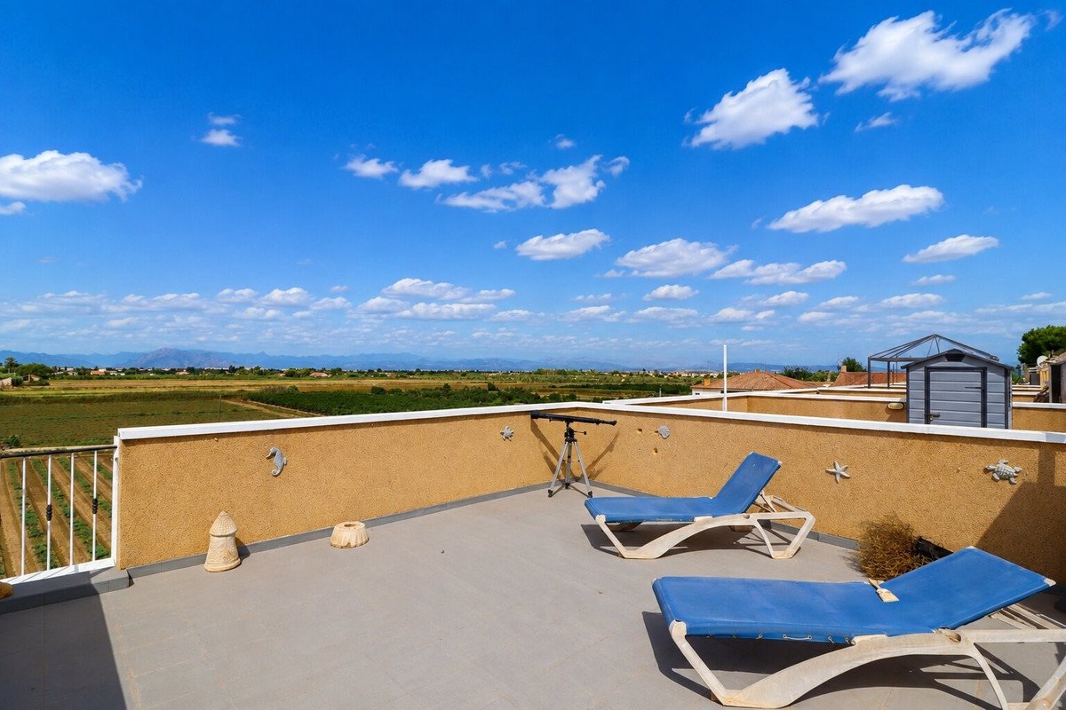 Rooftop terrace with lounge chairs, telescope, and scenic countryside view under a blue sky with clouds.