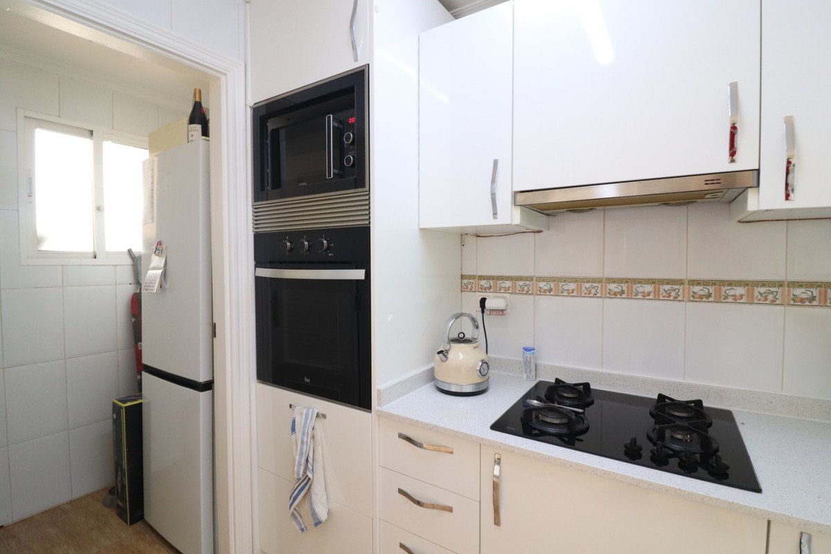 Modern white kitchen with built-in oven, microwave, and stovetop. Features a refrigerator and a window with natural light.
