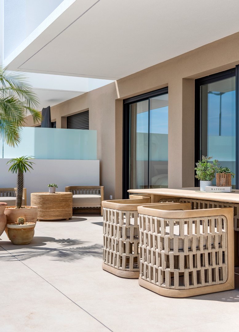 Modern terrace with comfortable seating, dining table, and potted plants, overlooking blue sky and modern building.