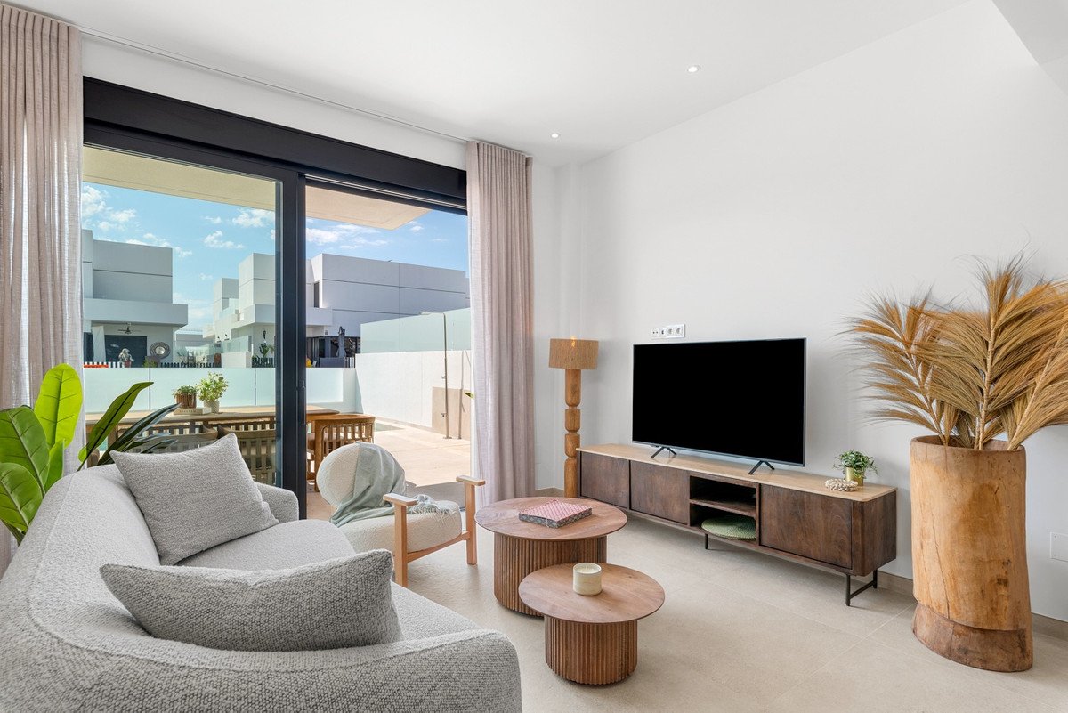 Modern living room with plush sofa, coffee tables, TV, and large sliding doors opening to an outdoor patio with a table and chairs.