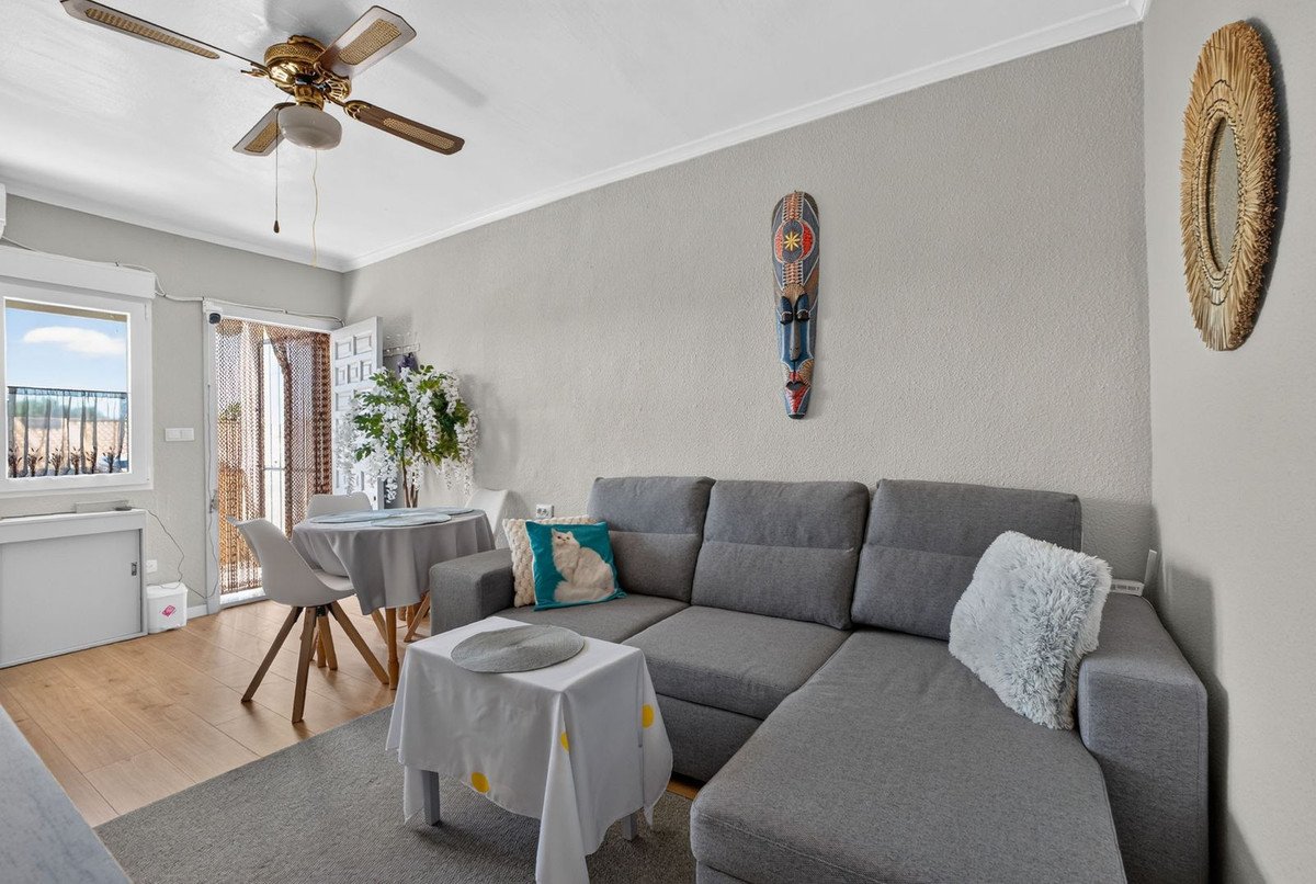 Modern living room with a gray sectional sofa, dining table, and window view. Features decorative African mask.