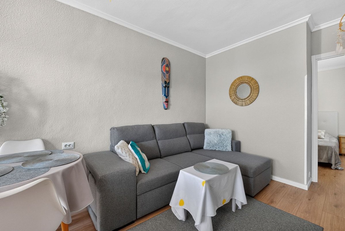 Modern living area with a comfortable grey sectional sofa, dining table, and decorative wall art, leading to a bedroom.