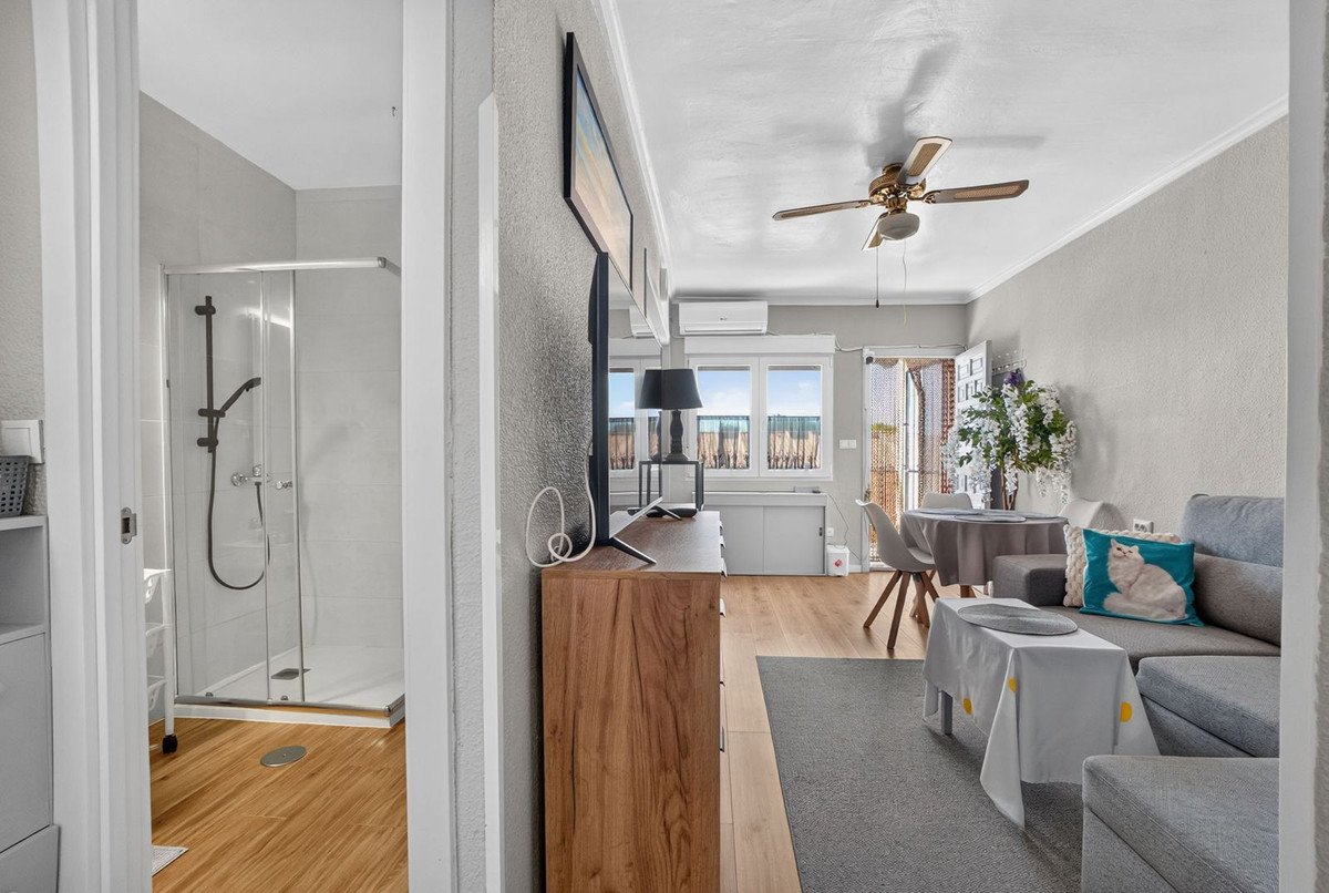 Modern living and dining area with a gray sofa, dining table, and a glimpse of a clean, modern shower room with glass doors open.