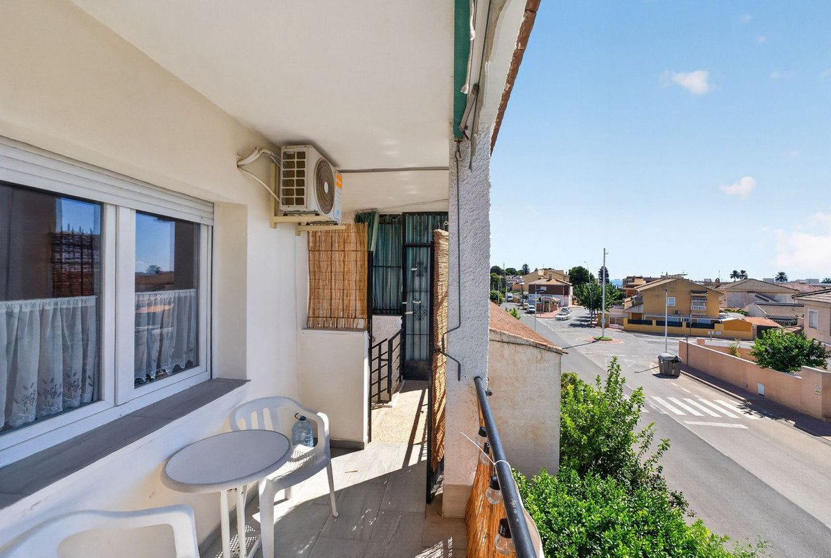 A balcony with a small table and chairs, offering a view of a residential street with houses.