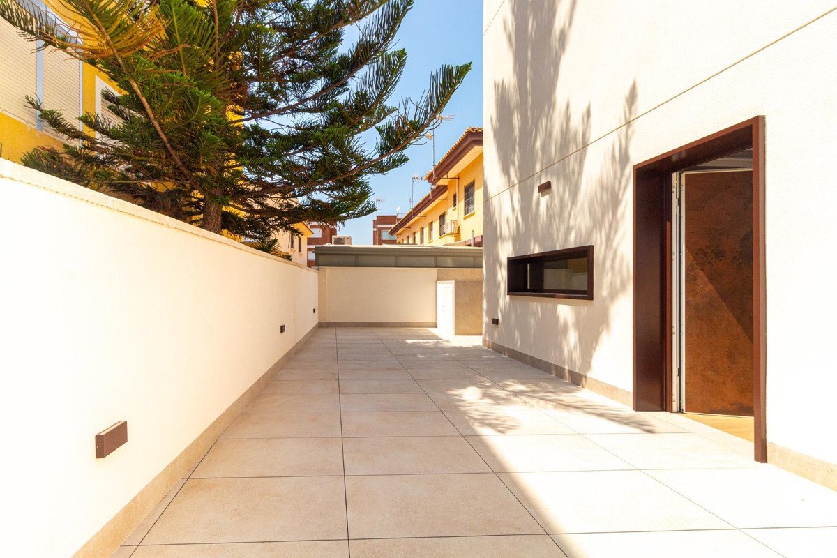 Spacious tiled terrace with a green tree, building facade, and an open modern door. Sunny day.
