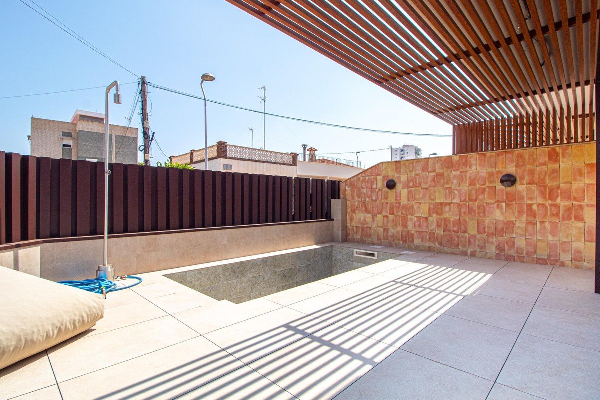 A modern patio area featuring a small pool, a wooden pergola casting striped shadows, and a beige outdoor cushion.