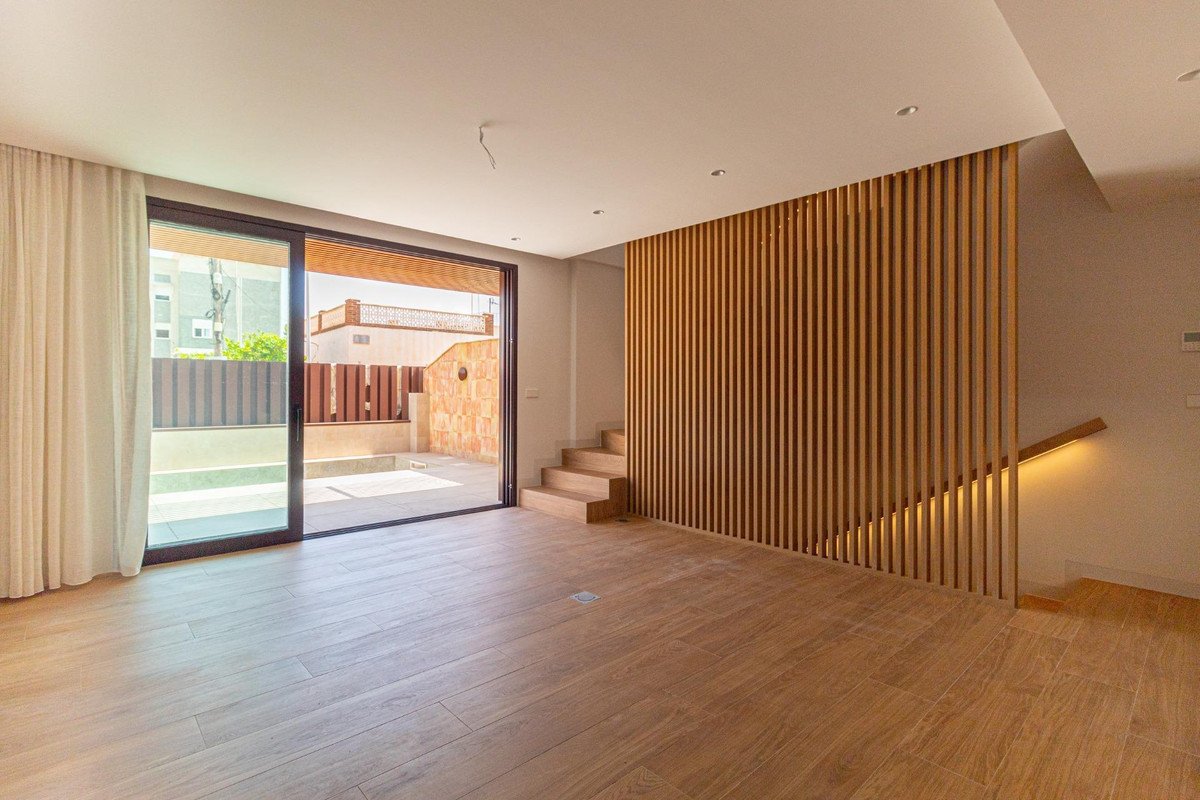 Modern living room with sliding glass doors opening to a pool and patio, featuring a slatted wood accent wall and stairs.