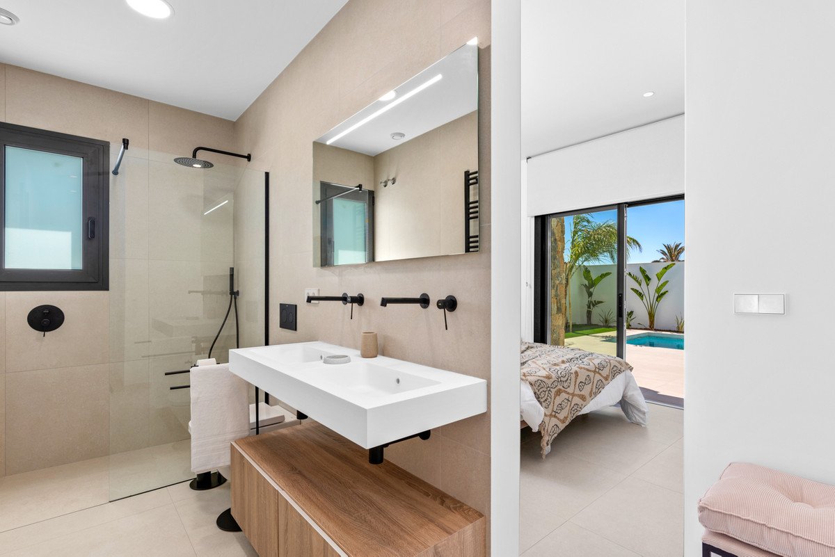 A modern bathroom features a double vanity, walk-in shower, and a view of a bedroom with a private pool and tropical plants.
