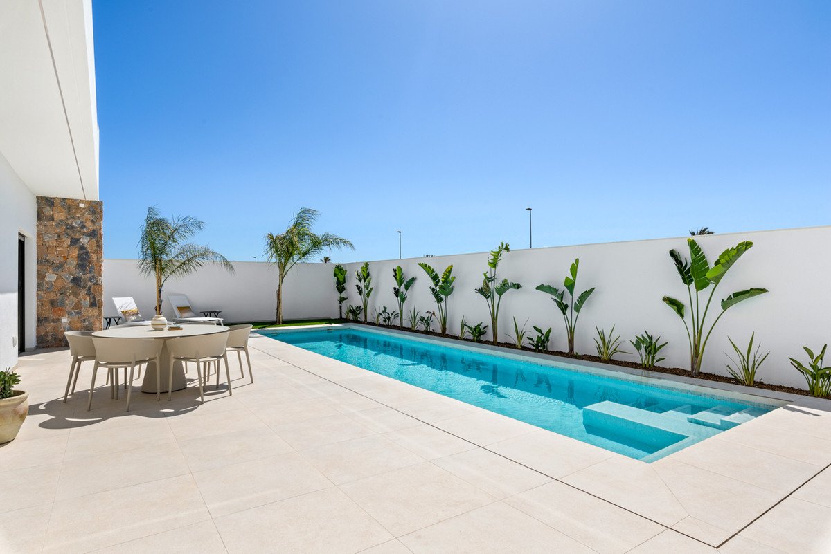 A modern backyard with a rectangular swimming pool, sun loungers, and an outdoor dining table with chairs.