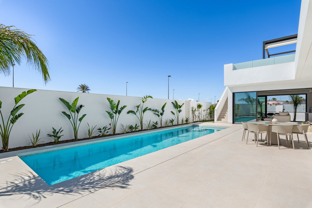 Modern villa exterior with a long swimming pool, terrace with dining table, and rooftop balcony.