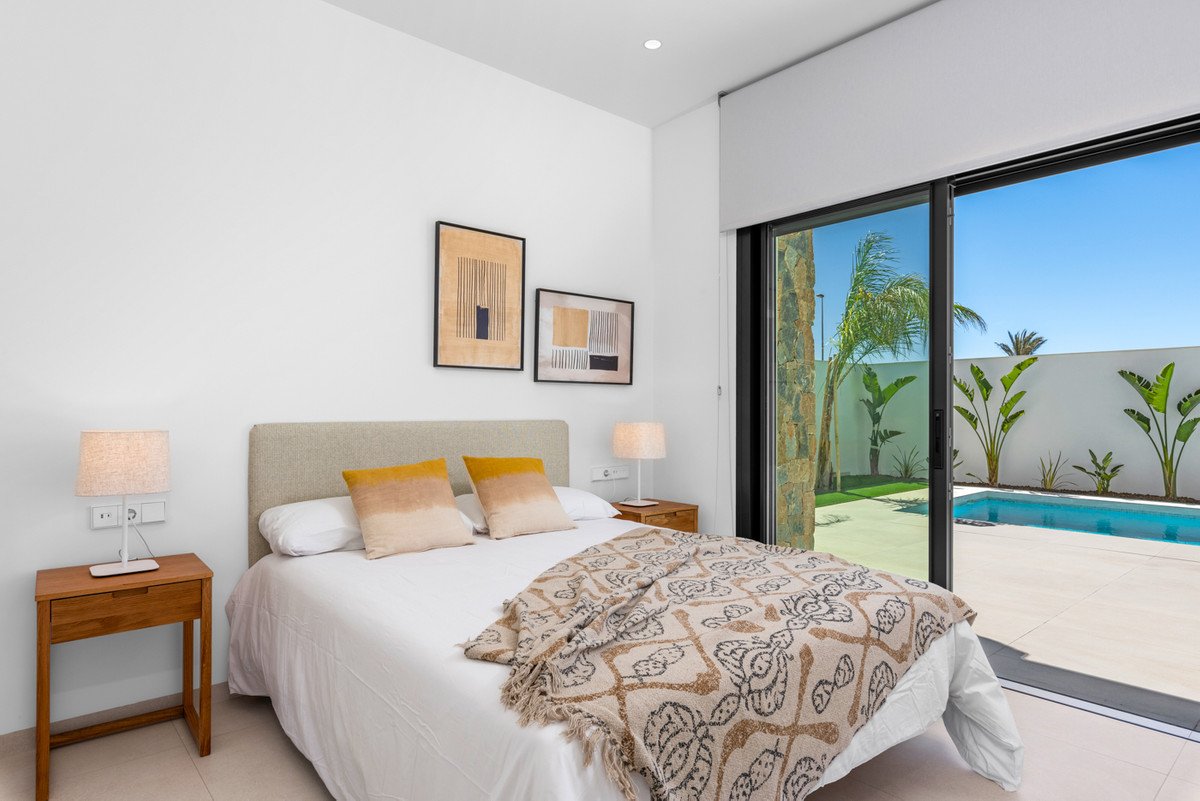 Bedroom with a view of a swimming pool and palm trees through sliding glass doors on a sunny day.
