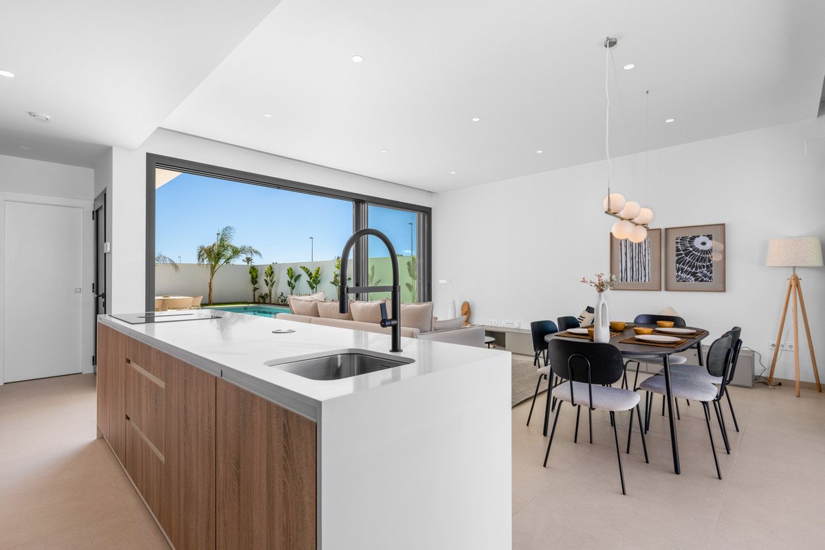 Modern open-plan living space with kitchen island, dining area, and living room, opening to a pool and garden view.