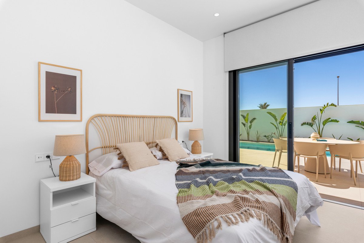 Bedroom with a bed, rattan headboard, and a view of a swimming pool and outdoor dining area through glass doors.