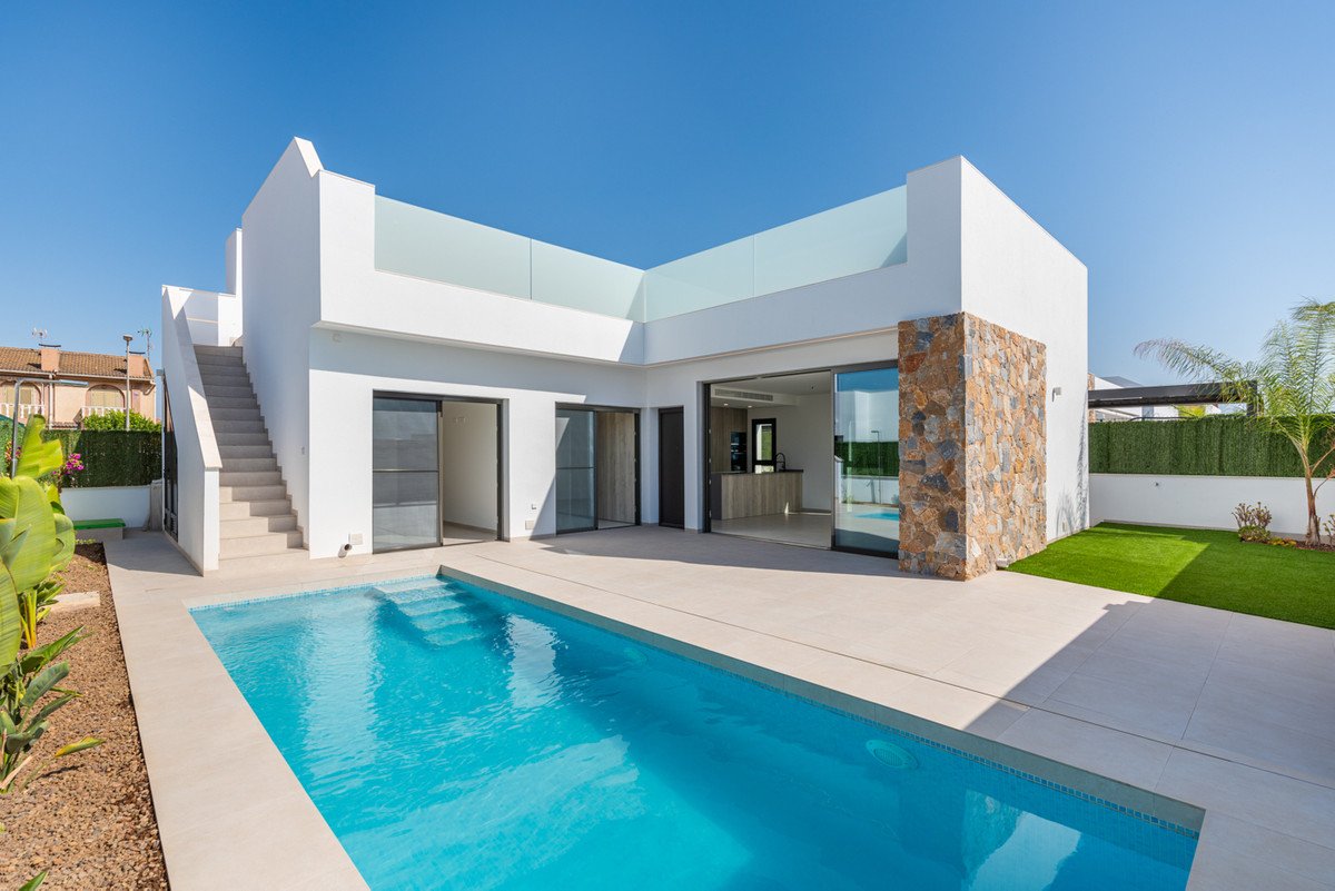A modern white villa with a swimming pool, outdoor seating area, and glass balcony railings under a clear blue sky.
