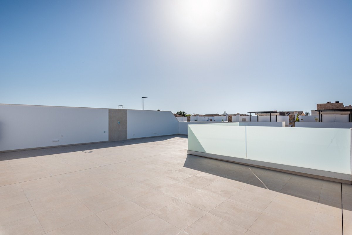 Spacious modern rooftop terrace with tiled floor, white walls, glass balustrade, and an outdoor shower with a clear blue sky.
